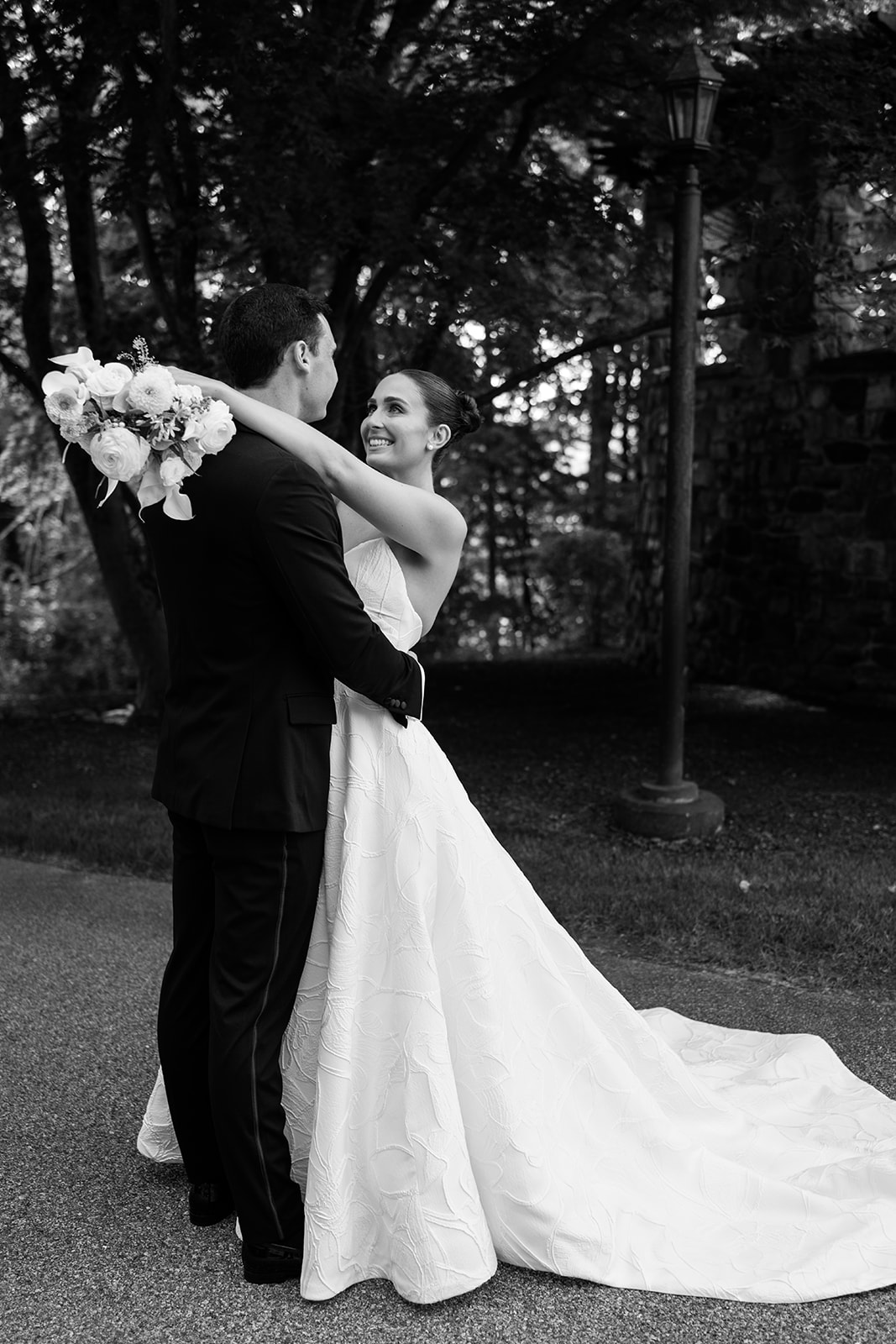 Black and white film portrait of a bride hugging her groom and looking up at him with a joyful smile.